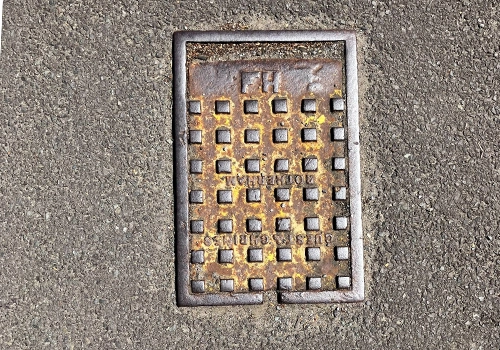 A metal rectangle cover on the floor, engraved with FH for fire hydrant and square detailing within the rectangle. 