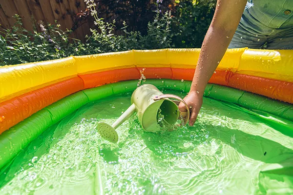 Person collecting water from a paddling pool using a watering can
