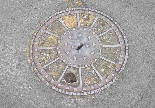 A metal circular wastewater cover with raised square detailing around the outside and centre. 
