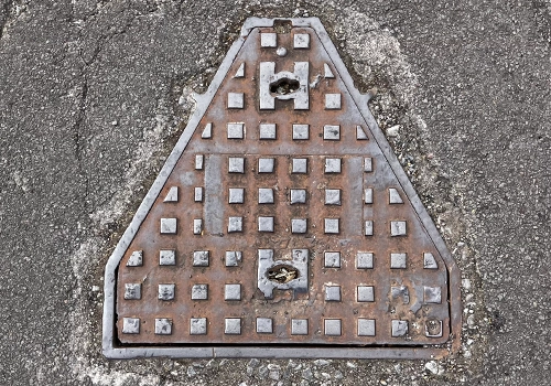 Triangular mental wastewater cover within the road, that has a raised square pattern.  